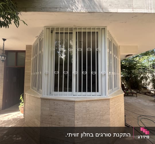 סורגים ישרים מברזל בצבע לבן המותקנים על חלון במבנה מרוצף אבן
